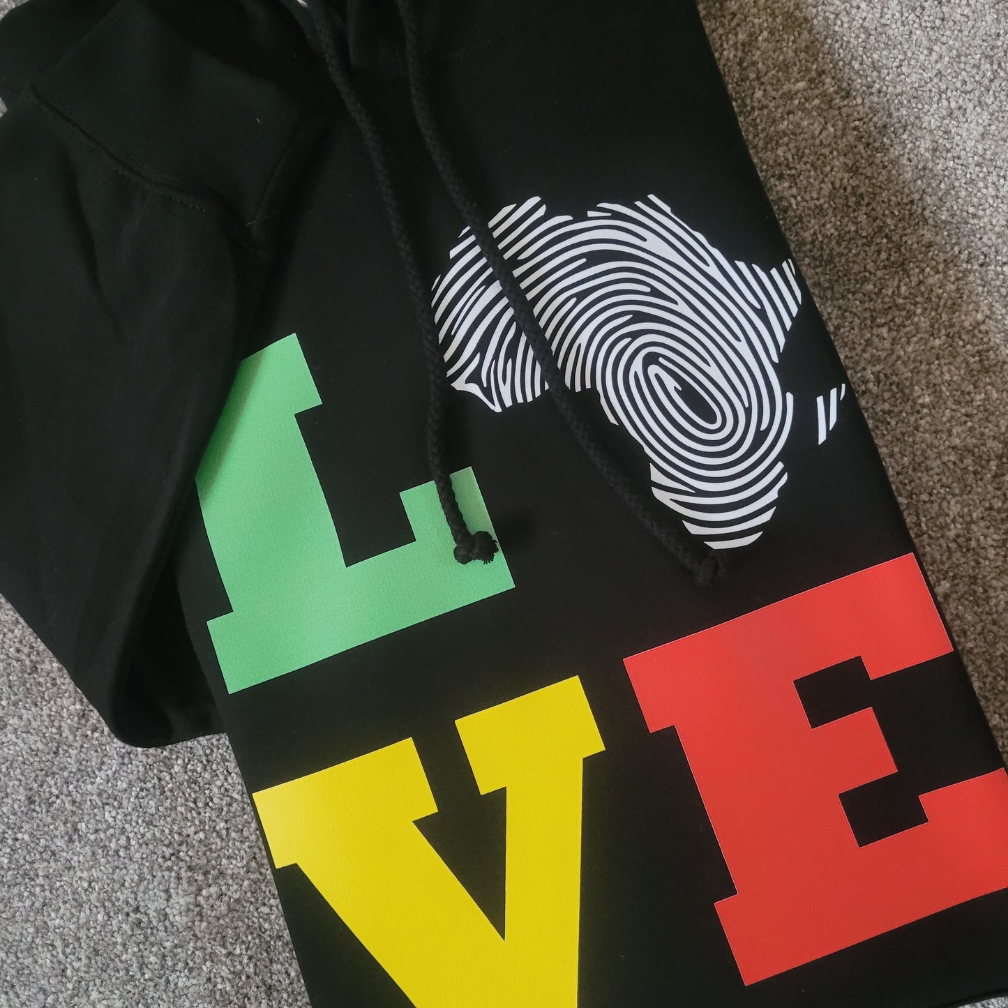 Close-up of black hoodie showing LOVE graphic with Africa fingerprint map and Pan-African colors red gold green, Afrocentric clothing detail.