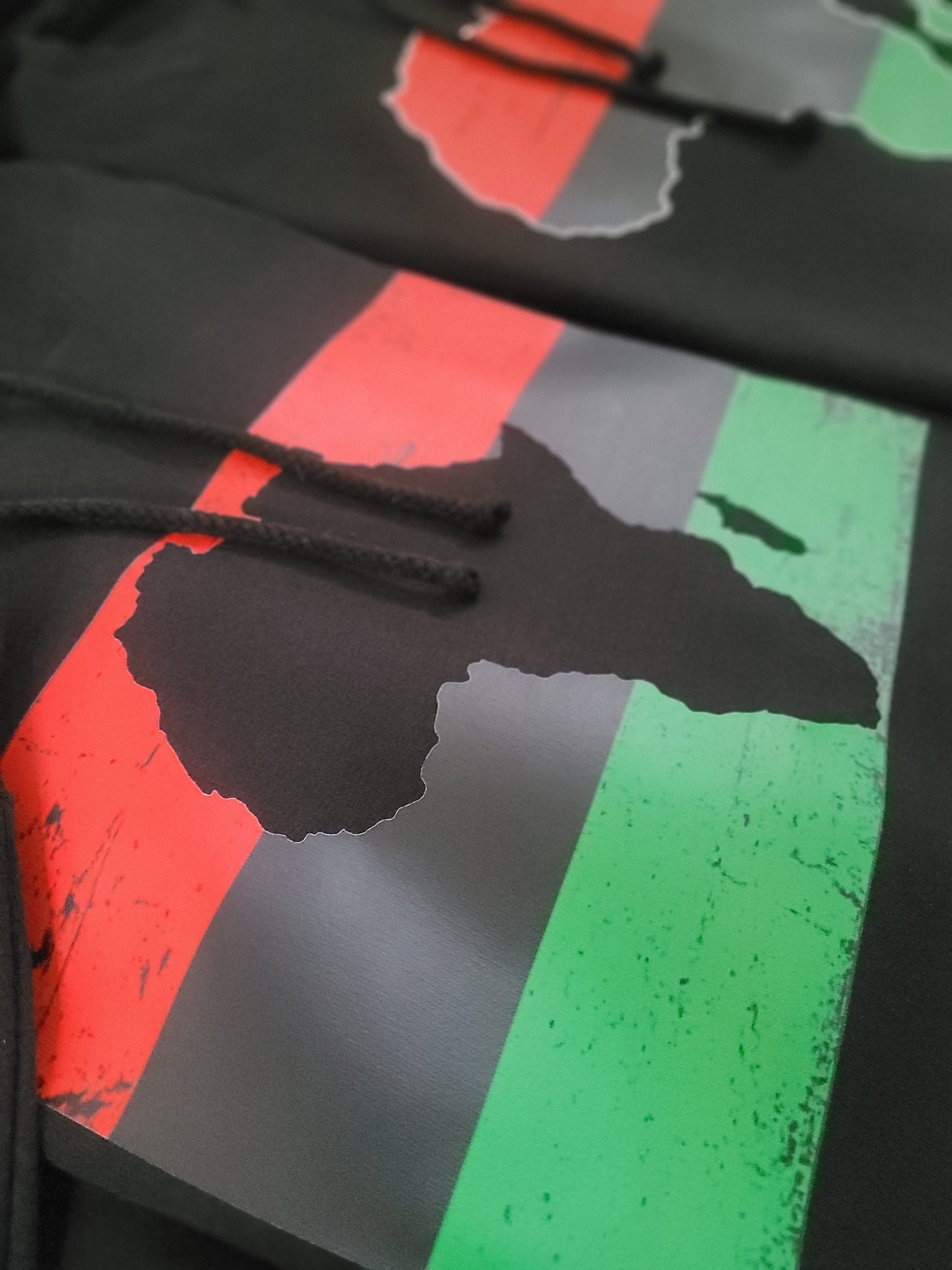 Close-up of black hoodie featuring Africa map silhouette over red, black, and green Pan-African flag stripes, Afrocentric clothing detail.
