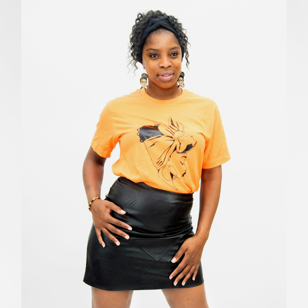 Black woman wearing orange afrocentric graphic t-shirt of woman wearing bow headwrap, paired with black faux leather mini skirt.