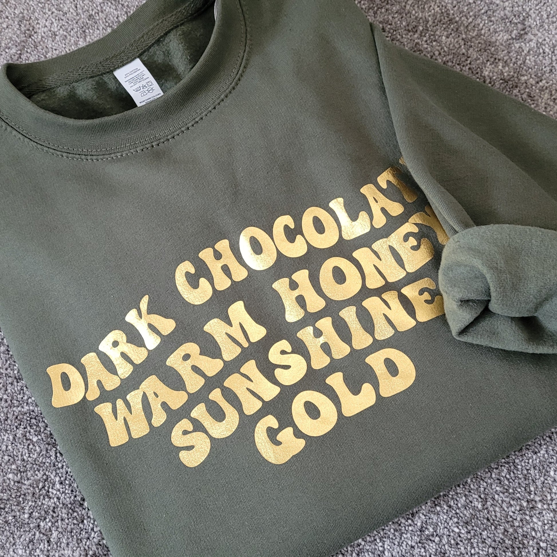 Olive green sweater with the phrase 'Warm Honey, Dark Chocolate, Sunshine & Gold' in metallic gold.